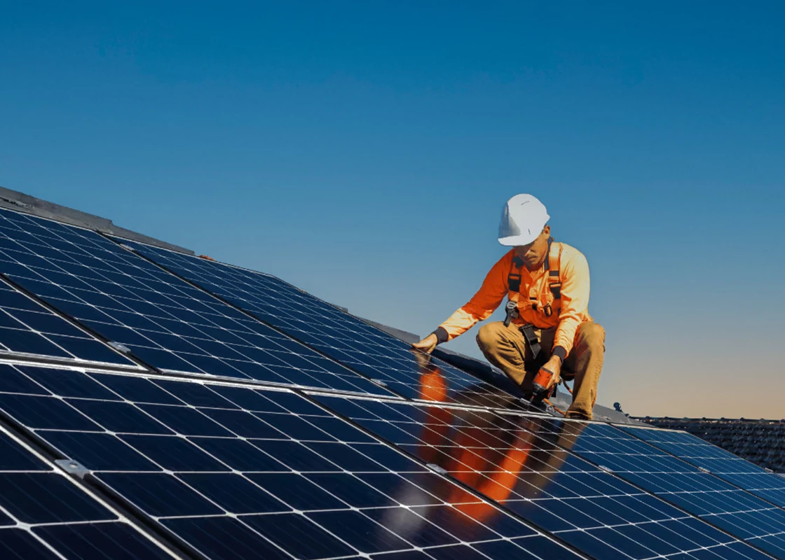 Un technicien portant un casque et un harnais de sécurité procède à la pose de panneaux solaires photovoltaïques sur un toit à Vichy par l'entreprise Charnet Électricité Générale.