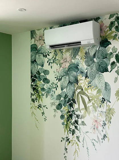 Installation soignée d'une climatisation réversible murale au-dessus d'un papier peint floral décoratif, réalisée par Charnet Électricité Générale.