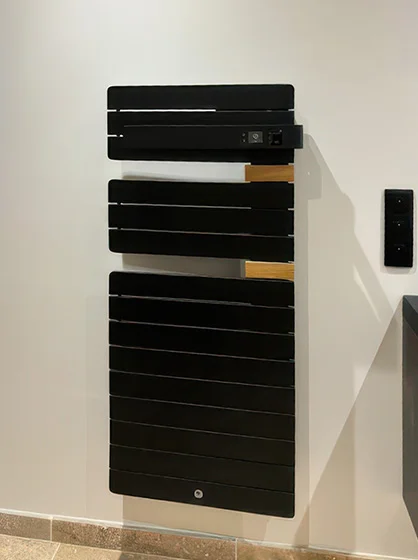 Installation d'un radiateur sèche-serviettes électrique noir design dans une salle de bain à Vichy par Charnet Électricité Générale.