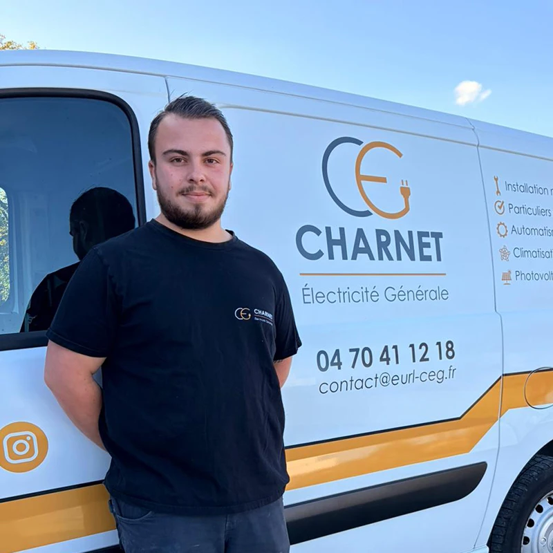 Artisan électricien, devant son véhicule utilitaire floqué au nom de Charnet Électricité Générale à Vichy.